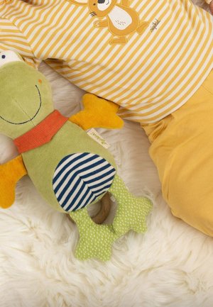 Un doux jouet en peluche vert en forme de grenouille avec un bandeau orange, un ventre rayé bleu et blanc, et des pattes vertes à motifs, reposant sur une surface en fourrure blanche.