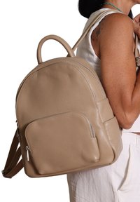 Zaino in pelle beige con forma arrotondata, due spallacci e una tasca frontale con zip e accessori in metallo argentato.