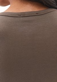 Brunt ribbat tyg med en fin strikkad struktur, med en enkel rund halsringning och fokus på baksidan av plagget.