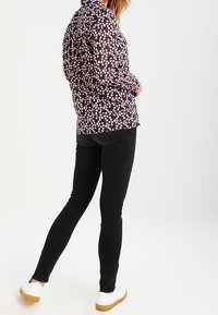 Langärmliges Shirt mit navyfarbenem Hintergrund und einem pinken Blumenmuster. Kombiniert mit schwarzen Skinny Jeans und weißen Sneakers mit braunen Sohlen.