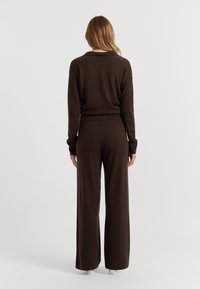 Bruine gebreide trui en wijde broek, met ribbelmanchetten, een relaxte pasvorm en een gladde textuur. Beide stukken zijn geschikt voor casual draag.