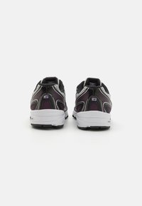 Baskets de sport noires et violettes avec panneaux en maille, accents réfléchissants et semelle blanche rembourrée. Présentent une finition texturée et un talon robuste.