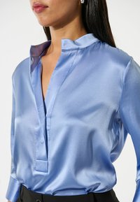 Lichtblauwe satijnen blouse met een moderne kraag, voorzien van een v-hals en een subtiele glans. Soepele textuur met lange mouwen.