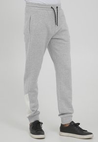 Gray sweatpants made of soft fabric, featuring an elastic waistband, side pockets, and a white accent on the lower leg. Black drawstring included.