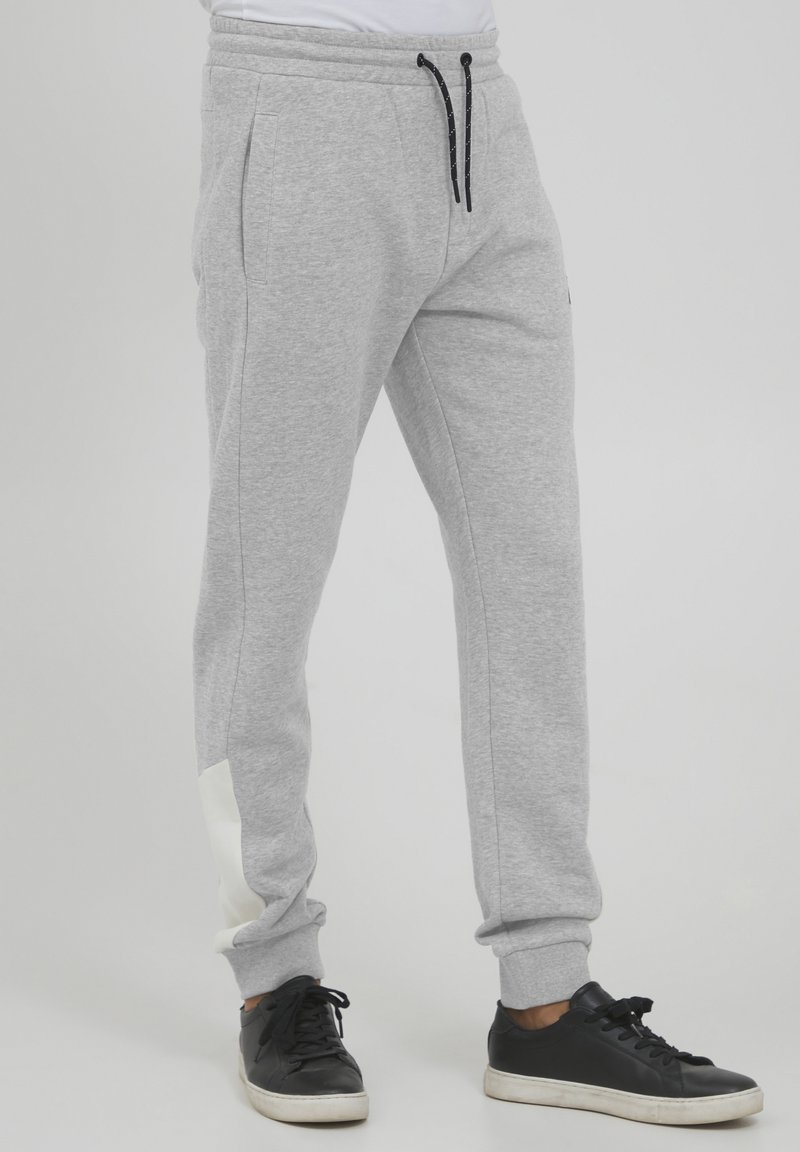 Gray sweatpants made of soft fabric, featuring an elastic waistband, side pockets, and a white accent on the lower leg. Black drawstring included.
