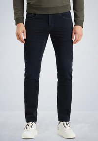 Jean bleu foncé avec une coupe slim, un design à cinq poches et une texture lisse. Associés à des baskets blanches avec des accents noirs.