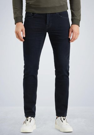Dark blue jeans with a slim fit, five-pocket design, and a smooth texture. Paired with white sneakers featuring black accents.