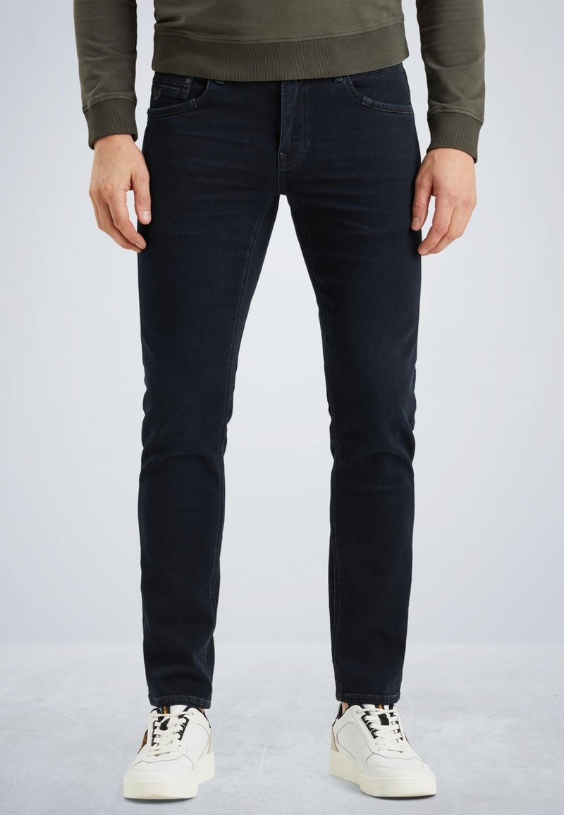 Jean bleu foncé avec une coupe slim, un design à cinq poches et une texture lisse. Associés à des baskets blanches avec des accents noirs.