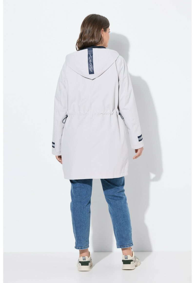 Veste légère grise résistant à l'eau avec capuche, taille élastique et accents bleu marine. Présente un logo au dos et des poignets rayés.