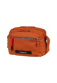 Sac à bandoulière orange de taille moyenne en tissu, avec une poche zippée à l'avant, une bandoulière réglable et une étiquette de logo noire.