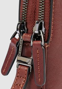 Dettaglio della cerniera di una borsa sintetica marrone con accessori metallici, caratterizzata da una finitura strutturata e cuciture a contrasto sugli accenti in pelle.