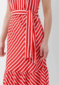Rot-weißer gestreifter Kleid mit enganliegendem Oberteil, einem gebundenen Gürtel in der Taille und einem ausgestellten, rüschierten Saum. Glatte Stofftextur.