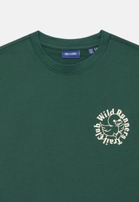 Ciemnozielona bawełniana koszulka z okrągłym dekoltem i kremową grafiką kaczki z tekstem "Wild Runners Club" z przodu.