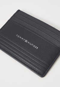 Portafoglio in pelle nera con più slot per schede, caratterizzato da un design testurizzato e dal logo "TOMMY HILFIGER" in bianco. Forma compatta e sleek.