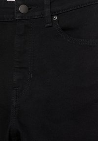 Prim-plan cu blugi negri din denim care arată talia cu nasture metalic, buzunarul frontal cu nit și detalii vizibile de cusătură.