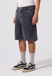 Shorts en velours côtelé gris avec une coupe décontractée, dotés de poches avant et d'une fermeture à bouton, associés à des chaussettes grises et des baskets noires.
