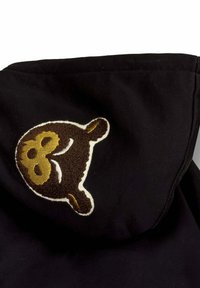 Sudadera negra con un logo de oso bordado en marrón y dorado en la capucha, con una textura suave y un borde crema contrastante.