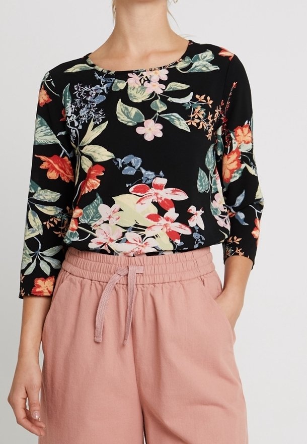 Top nero a fiori con maniche a tre quarti che presenta fiori e foglie di vari colori; abbinato a pantaloni rosa chiaro con vita elasticizzata.