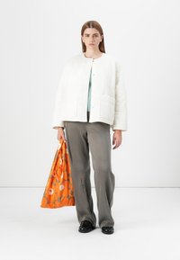 Bijela prošivena jakna sa kopčom na pritisak i prednjim džepovima, slojevito nošena preko svijetloplave majice. Sive hlače s suptilnim uzorkom i narančasta torbica s cvjetnim dizajnom.