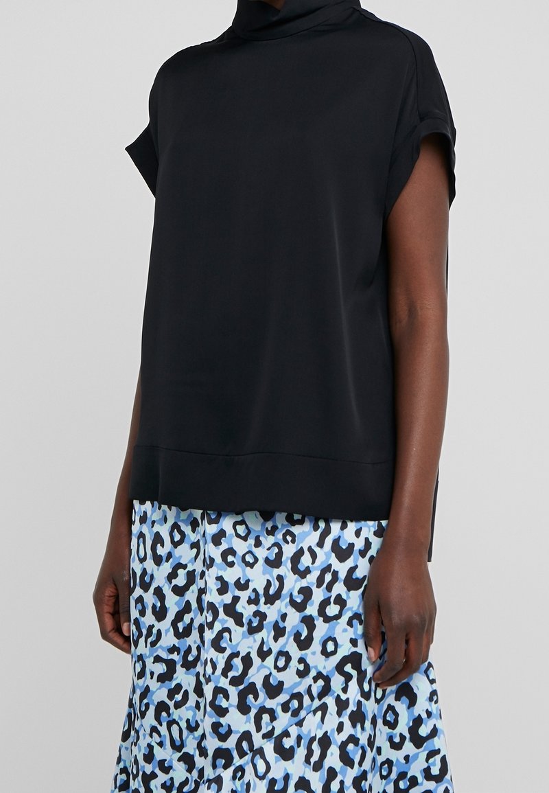 Haut noir à manches courtes avec un col montant ; tissu lisse. Associé à une jupe en imprimé léopard bleu. Design simple et moderne avec une coupe droite.