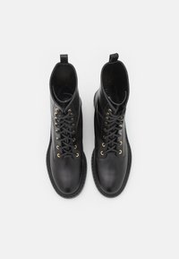 Botas de tobillo de cuero negro con ojales dorados, punta redonda y diseño de cordones. Cuentan con una agarradera en la parte posterior y una suela texturizada.