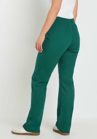 Groene katoenen joggingbroek met een relaxte pasvorm, elastische tailleband en rechte pijpen. Gecombineerd met witte sneakers en een eenvoudig topje.