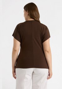 Camiseta marrón de manga corta con cuello redondeado, textura suave y un diseño sencillo. Los detalles de la camiseta incluyen una costura en la parte posterior y un corte relajado.