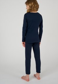 Navy geribbeld longsleeve shirt met ronde hals en bijpassende fitted broek, beide rekbaar en zacht, van achter bekeken.
