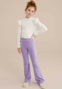 Valkoinen pitkähihainen paita, jossa on röyhelöolkaimet, ja violetit ribbikankaiset leveät housut. Tyttö poseeraa yksi käsi lanteellaan. Vähän kuvioita.