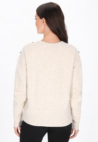 Jasnobeżowy sweter o miękkim, teksturowanym wykończeniu, z okrągłym dekoltem i ozdobnymi czarnymi guzikami na szwach ramion.