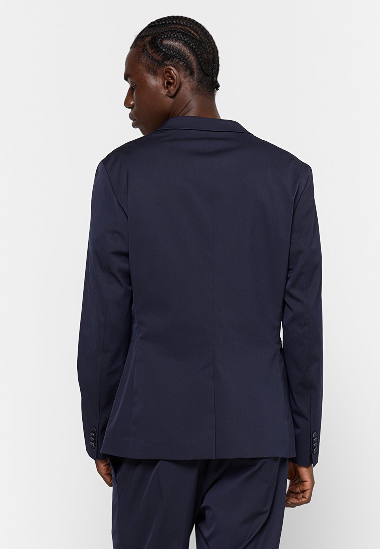 Blazer bleu marine avec un design structuré, devant à simple boutonnage, revers en pointe et poignets boutonnés. Texture lisse et coupe ajustée.