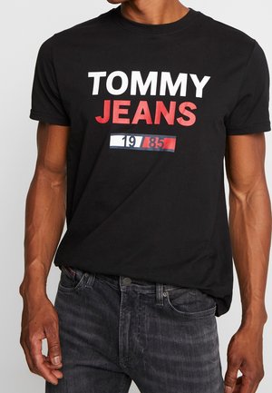 Czarna bawełniana koszulka z wyrazistym białym i czerwonym napisem "TOMMY JEANS" oraz grafiką w kolorach czerwonym i niebieskim, okrągły dekolt, krótkie rękawy.