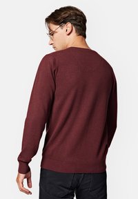 Bordowy sweter z miękkiego materiału, z okrągłym dekoltem, ściągaczami przy rękawach i u dołu, oraz gładką fakturą. Widok z tyłu.