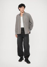 Camicia a quadri grigia con taschino sul petto, abbinata a jeans in denim neri a gamba larga con strisce laterali e sneakers nere.
