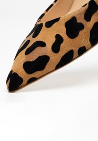 Pompe en daim imprimé léopard, bout pointu, construction légère, avec des taches noires irrégulières sur un fond tan, texture lisse.