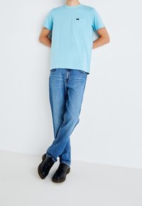 Ljust blå bomulls-T-shirt med en ficka, i kombination med urtvättning blå denimjeans och svarta läderskor med en strukturerad sula.