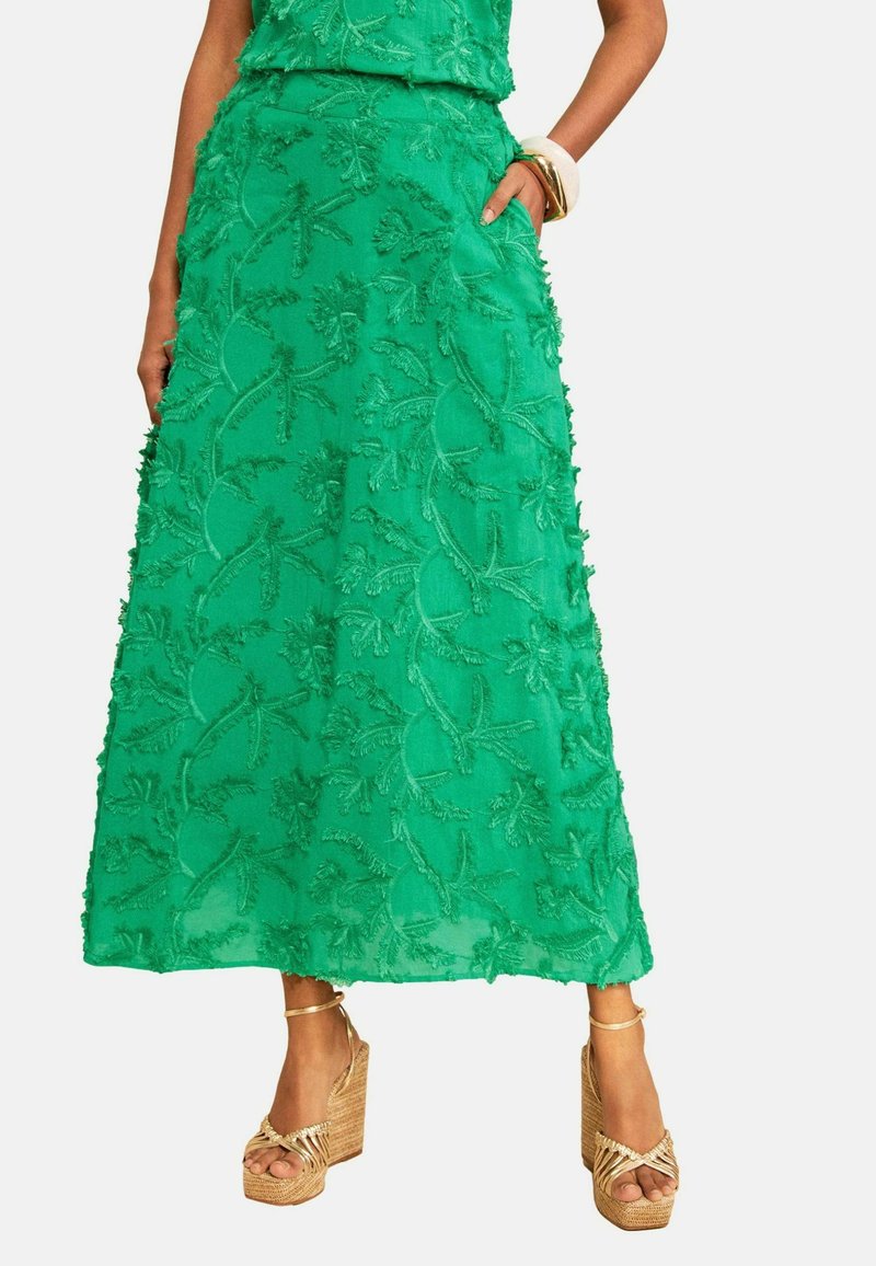 Green textured A-line skirt with floral patterns, worn with gold platform sandals and chunky bracelets on the wrist.
