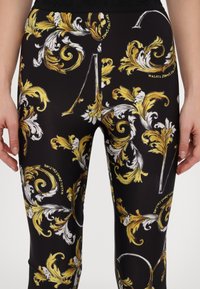 Mustad mustad mustikad, millel on keerukad kullavärvi ja valged lillemustrid. Materjal näeb välja sile ja vormi ümbritsev disain. Lähivõte näitab detaile.