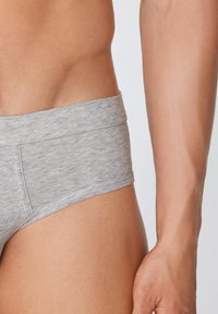 Šedé bavlněné boxerky bez švu v pase, které nabízejí příjemnou texturu a elegantní design, částečně viditelné na boku s přirozeným tónem pleti.