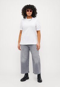 White short-sleeve t-shirt with round neck, paired with gray loose-fitting jeans and black ankle boots. Model wears pink sunglasses.