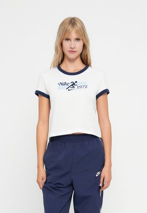 Crop top in cotone bianco con colletto e maniche a coste navy. Caratterizzato dal logo "Nike 1972" in stampa grafica blu. Abbinato a pantaloni da jogging navy.