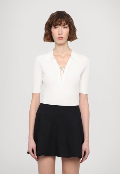 Haut blanc à rayures avec des manches courtes, col et devant lacé, associé à une jupe noire évasée. Texture lisse ; design simple.