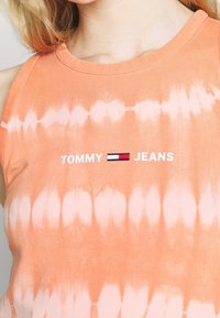 Top sin mangas de color naranja con estampado tie-dye y el logotipo en blanco de "TOMMY JEANS". El material es algodón suave con una textura lisa, con un escote redondeado.