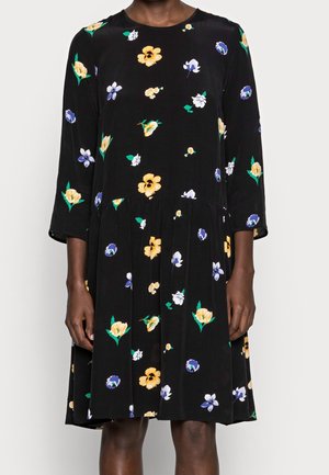 Schwarzes knielanges Kleid mit gelbem, weißem und lila Blumenmuster, dreiviertel Ärmeln und geraffter Taille, getragen von einer Person.