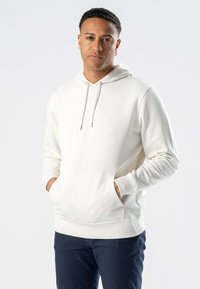 Hvid hoodie lavet af blødt stof med en kengurulomme, snøre i hætten, ribbede manchetter og en afslappet pasform, parret med mørke bukser.