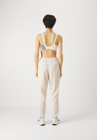Weißer Sport-BH mit schwarzen Streifen, kombiniert mit hellrosa Jogginghosen. Besitzt einen lockeren Schnitt und einen elastischen Bund. Sneakers runden das Outfit ab.