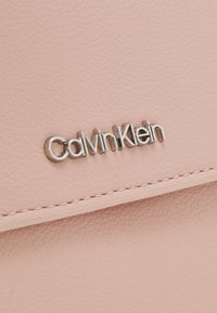 Portafoglio in pelle rosa Calvin Klein con superficie testurizzata, accentuato da un logo in argento e dettagli cuciti lungo i bordi.