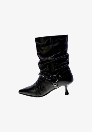 Stivale alla caviglia in pelle nera con design morbido, punta affusolata e tacco alto slim. Presenta un accento a catena attorno alla caviglia con un dettaglio in fibbia.