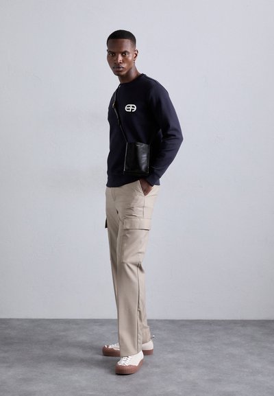 Tenger�észeti pulóver logóval, bézs cargo nadrág és bézs sportcipők struktúrált talppal. Fekete keresztpántos táska sima felülettel.