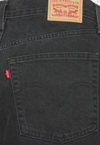 Poche arrière d'un jean Levi's noir avec une étiquette en tissu rouge et un patch en cuir avec logo et texte.